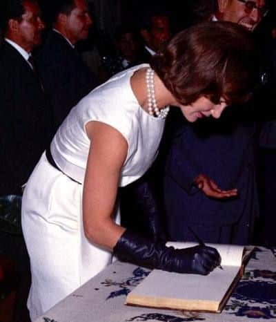 gloves become less popular - jackie kennedy signing a book wearing a white shift dress and black 3/4 gloves