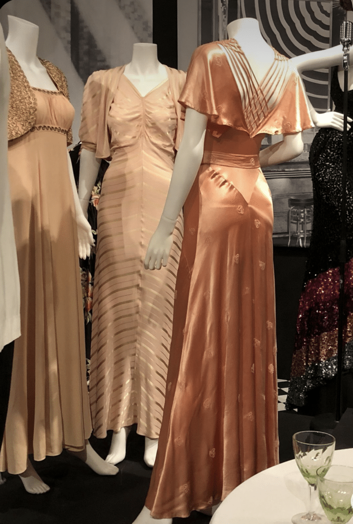 gatsby era - 3 mannequins with satin 1930's dresses on display, gold tones