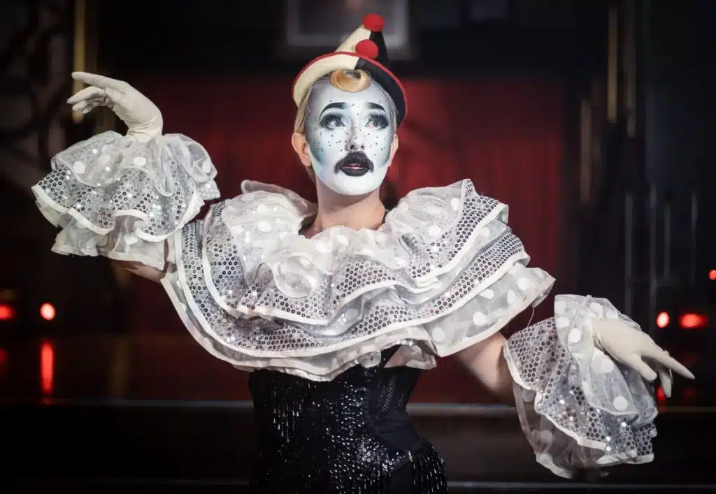 we love to play dressups - woman on stage wearing clown/joker minstrel costume and mustache 