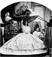 victorian era - women standing around whilst one is taking off a damaged petticoat from another woman 