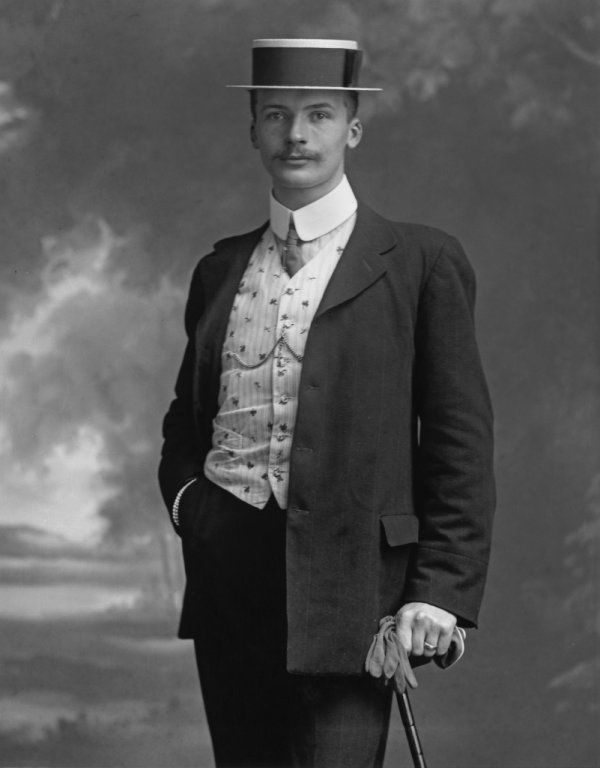 the edwardian gentleman - man in a boater hat and suit with contrasting waistcoat and shirt holding a walking stick