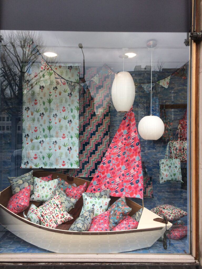 diy fashion - shop window depicting fabrics draped in a boat with cushions in various colours and designs