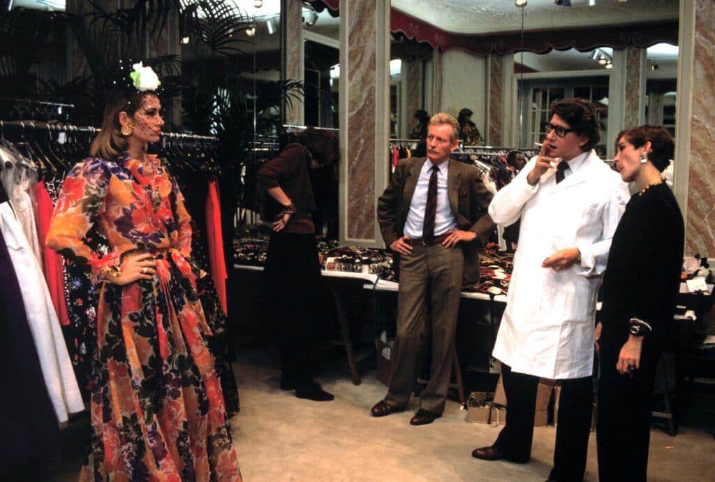 reviving past styles - yves saint laurent at a design studio 1983 admiring a models dress