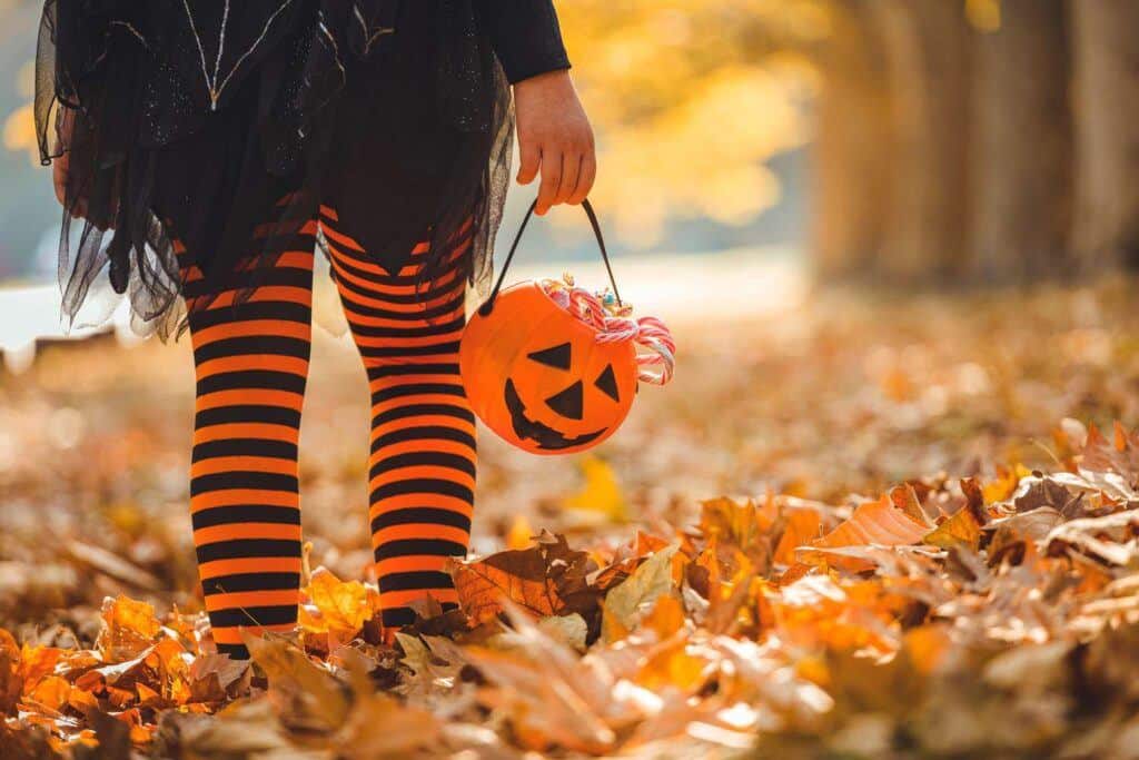 pop culture influence - child walking amongst autumn leaves wearing witch costume and carrying sweets bag