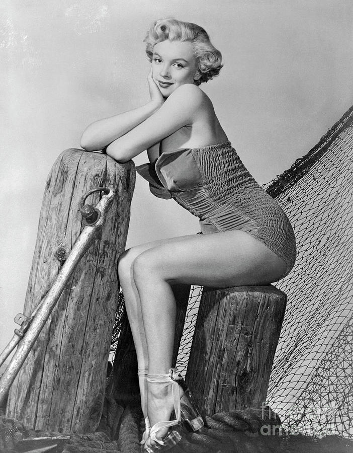 Marilyn Monroe sitting on a timber posts posing in ruched bathers and platform stilettos