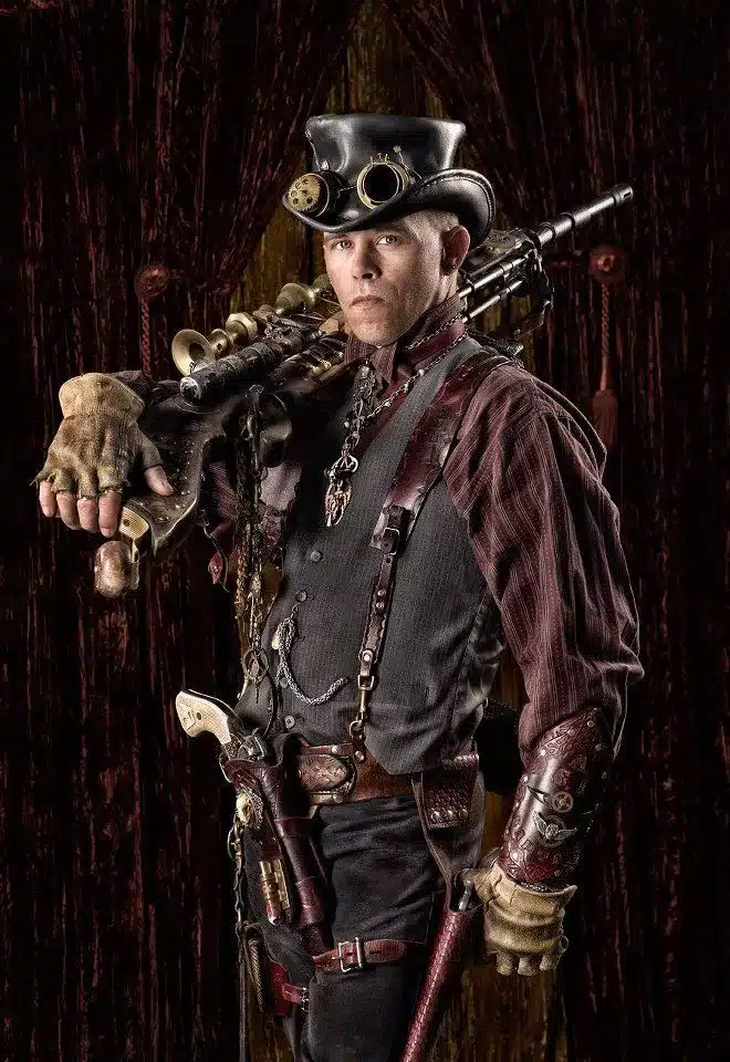 tips for using high quality steampunk attire - cowboy looking steampunk man with many straps, chains, belts and a gun holster holding a steampunk adorned rifle