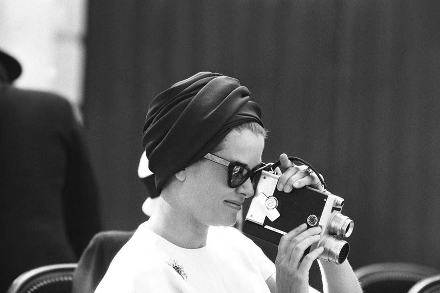 the impact of fashion's golden age icons - grace kelly lwearing a turban hat looking into a vintage film camera