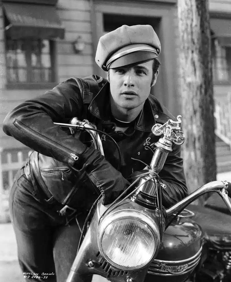 the impact of fashion's golden age icons - marlon brando leaning on a motor bike in leathers and news boy cap