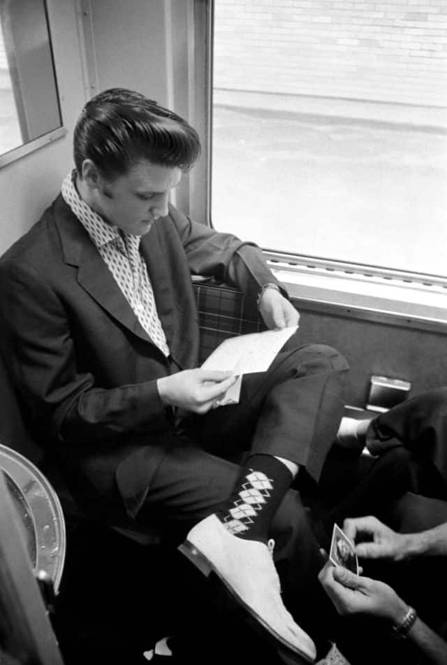 the impact of fashion's golden age icons - elvis presley reading a letter sitting in a waiting room in suit and white shoes