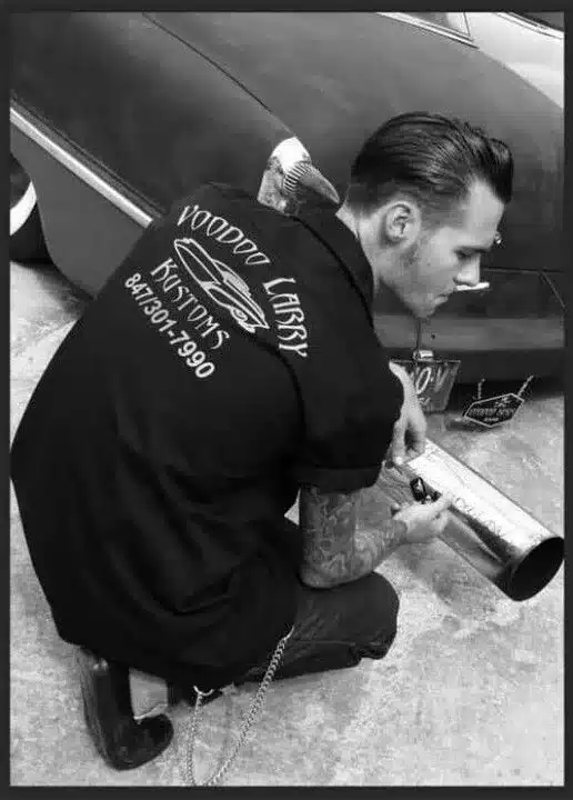 current rockabilly fashion trends - what's hot in today's scene, for men, man working on an exhaust in garage sporting tattoos, pompadour hair and black clothing