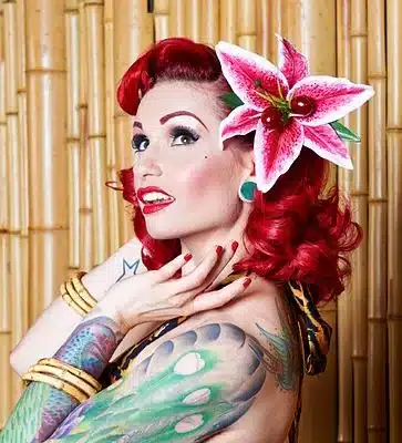 key elements of rockabilly fashion, statement jewellery - woman wearing cane bangles, large hair flower sporting arm tattoos and bright red hair