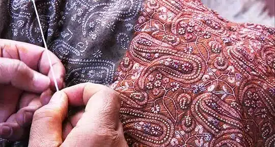 hand sewn elements and craftsmanship in materials - artisan hand sewing kashmir garment