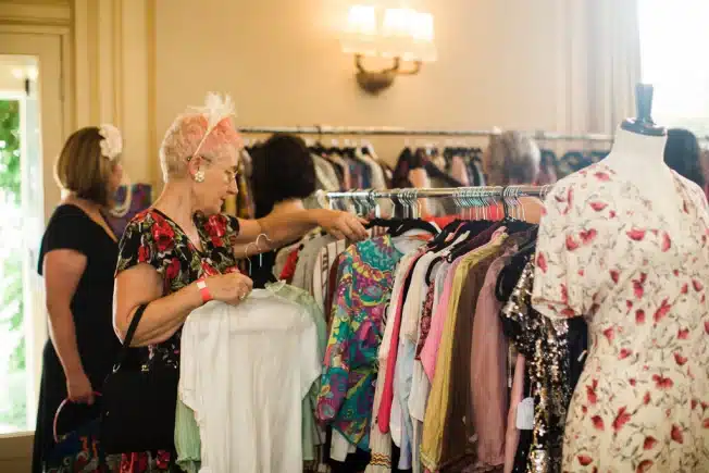 how to spot authentic vintage clothing, attending estate sales - lady sorting through a rack of clothing at estate auction