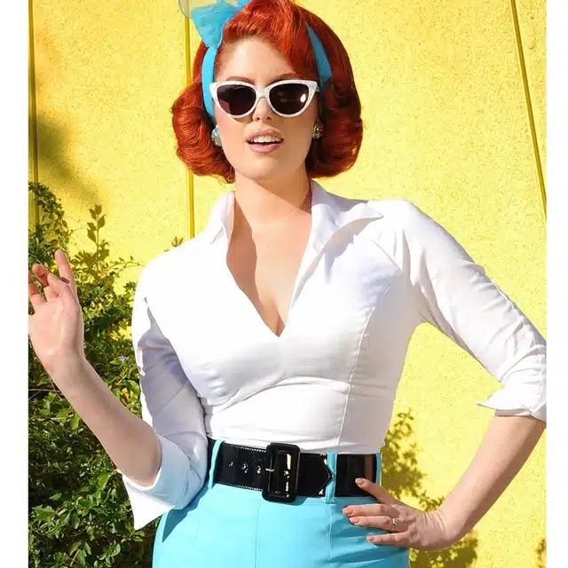 how to incorporate vintage  elements without looking outdated, woman in 50's retro outfit - wide belt, narrow pans and white shirt with cat-eye sunnies