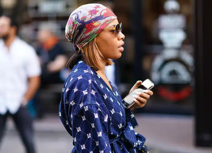 vintage workwear essentials - from practicality to empowerment - african/american woman holding phone dressed in paisley floral headscarf and blue tunic blouse