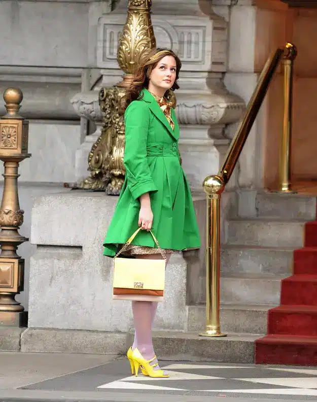 Fashion designers turning back the clock with current trends - woman outside historic building wearing a green trench coat with yellow shoes and accessories