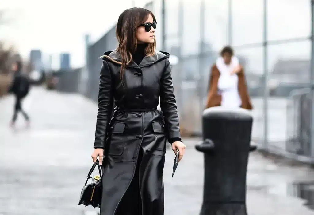 What's past is reborn in fashion styling - woman walking on a bridge wearing a black leather coat and black turtleneck jumper and sunglasses