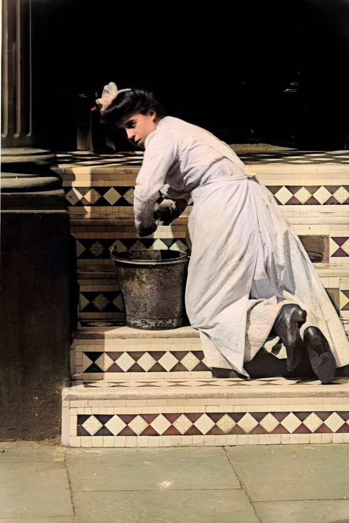 Edwardian woman kneeling on steps to rinse something in a metal bucket