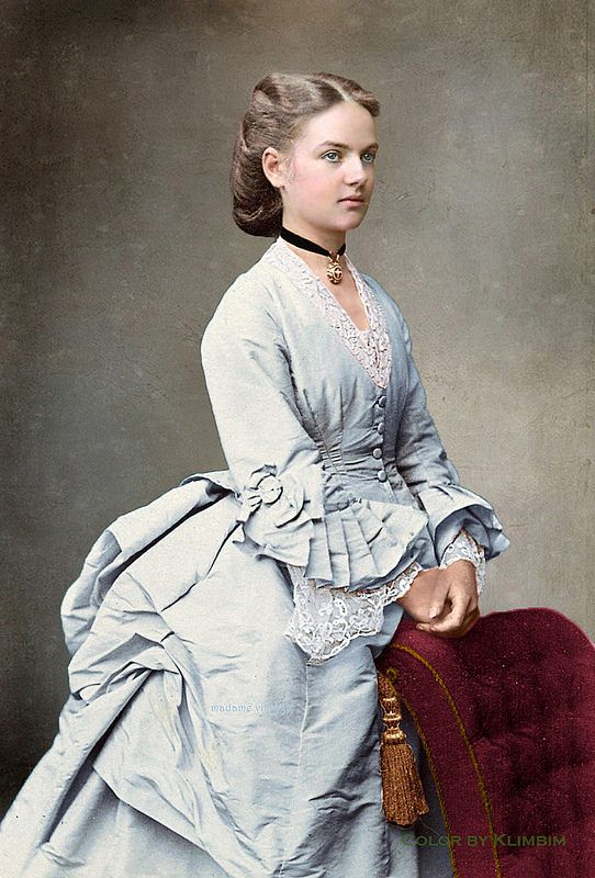 Woman from 1880's in period dress with large rear bustle and pleating on sleeves - v-neck blue dress