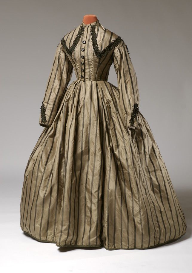 Early Victorian dress displayed in khaki colour with short neckline, fitted waist and tailored bodice trimmed in black piping cord
