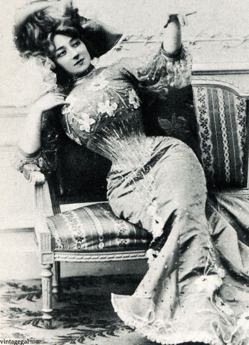 Edwardian woman on a sofa leaning sideways and wearing a very tight cinched waisted long dress