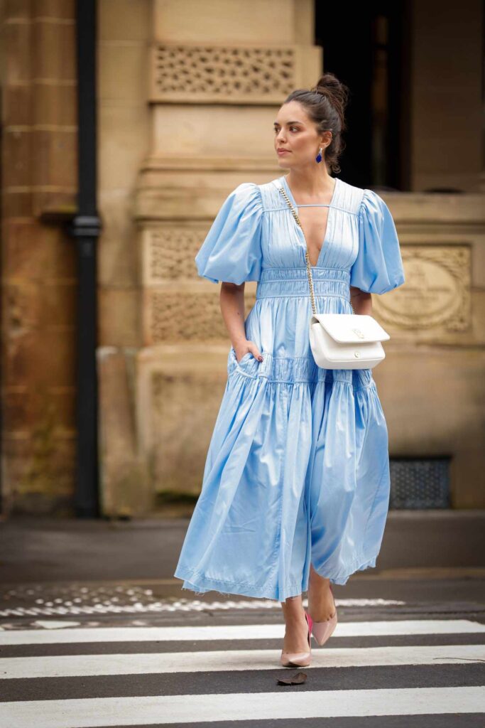 Girl wearing a flowing blue dress with puffy sleeves and across body evening bag