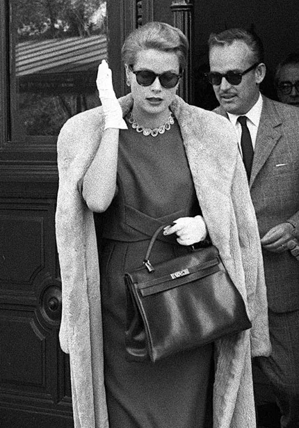 grace kelly dressed in a coat over a dress walking with her husband rainier