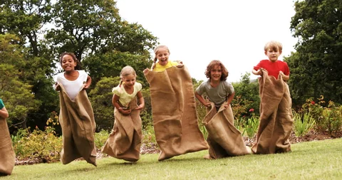 5 kids in a sack race on a garden lawn