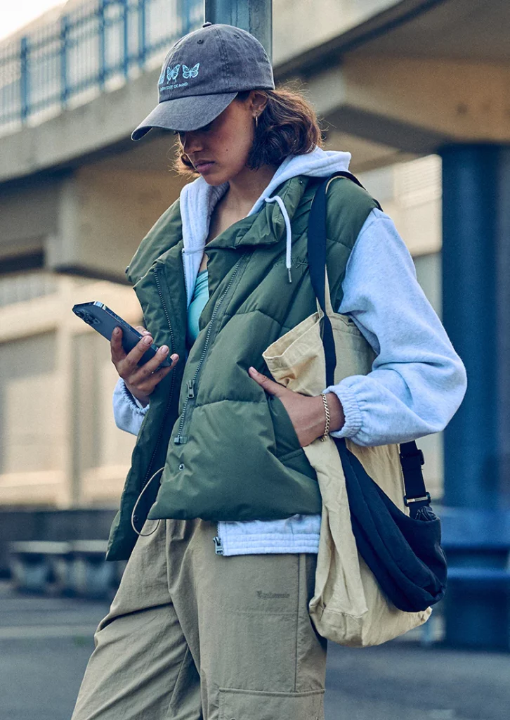 Girl holding a mobile phone in a padded khaki vest, cap and beige cargo pants