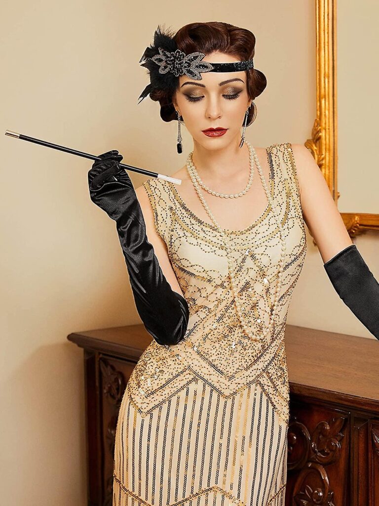 lady in a gold sequinned and tassle gatsby style dress with long gloves headband holding a cigarette spacer