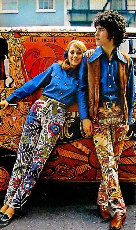 Man and woman leaning against a decorated van wearing blue shirts flower style fitted pants and a vest