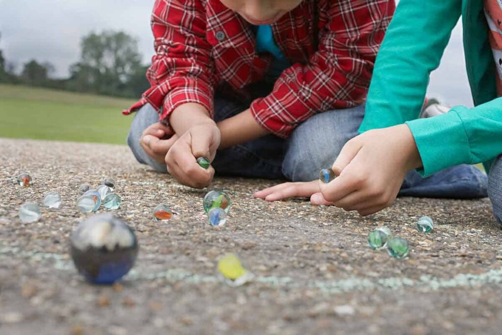 2 boys playing with marbles on bitumen