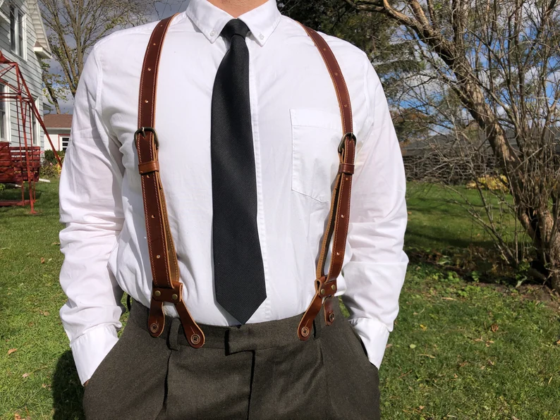 man wearing vintage leather suspenders secured by buttons over white shirt and black tie