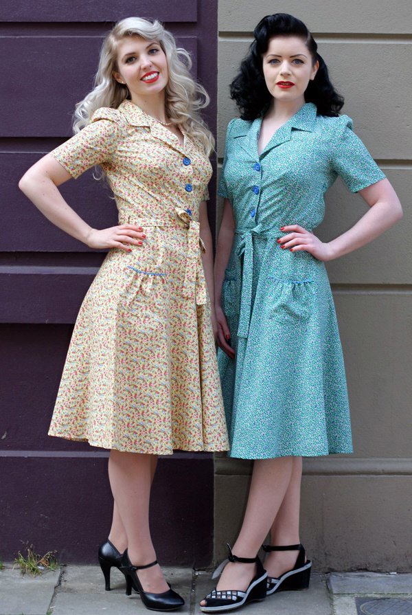 2 ladies in 1940's floral dresses and black shoes one blonde and the other brunette wearing same dresses in different colours