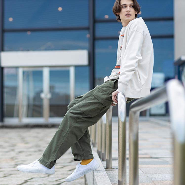 Guy sitting on a rail with khaki green cargo pants and white jacket