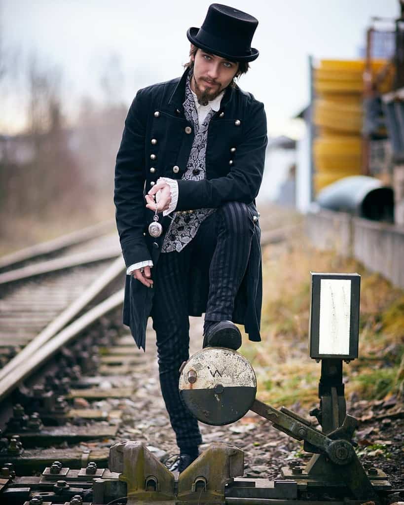 Man standing against a railway signal with top hat long coat striped pants and a pocket watch