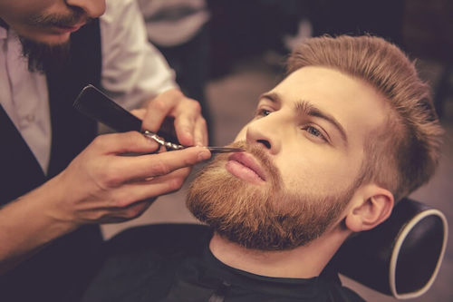 A bearded man getting his beard shaped in a barbers shop