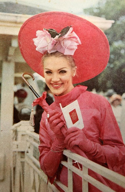 Lady wearing a 60's high neck dress with matching long gloves and straw hat pushed back with rose flowers