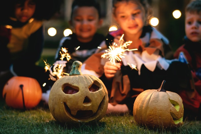 children lighting up sparklers near jack o lanterns at a community gathering