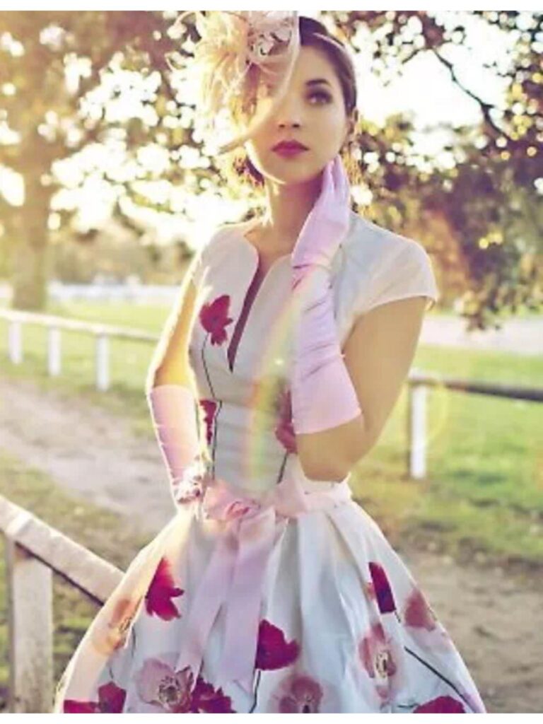 Lady in a white floral cap sleeve dress with long pink gloves and fascinator