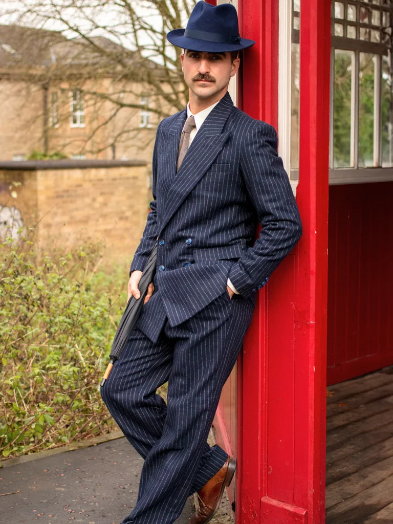 Man dressed in navy double breasted suit and trilby hat with tie and accessories