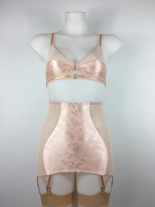 Mannequin wearing a 1930's or 1940's style set with bra suspender girdle and being stockings in a sating apricot tone