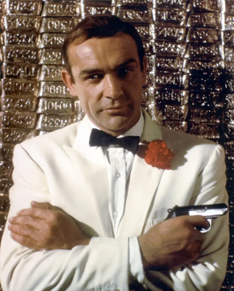 Sean Connery holding a pistol dressed in a white sports coat with a red carnation