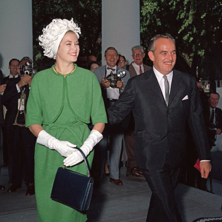 Grace Kelly and Prince Rainier in a black suit with Grace in a green dress suit with white gloves and hat