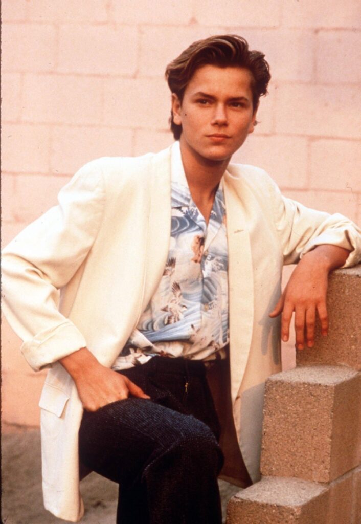 Man wearing a hawaiian style shirt and dark pants with rolled up sleeved blazer