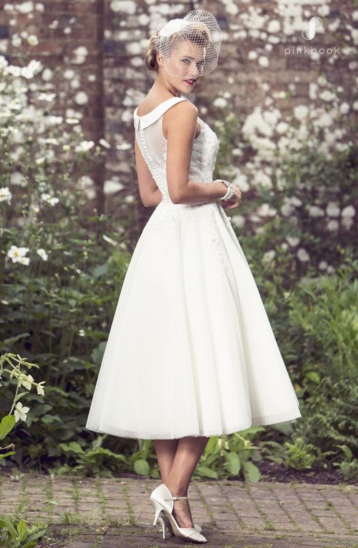 Bride in off white tea length dress pearl jewelelry and a fascinator in her updo hairstyle