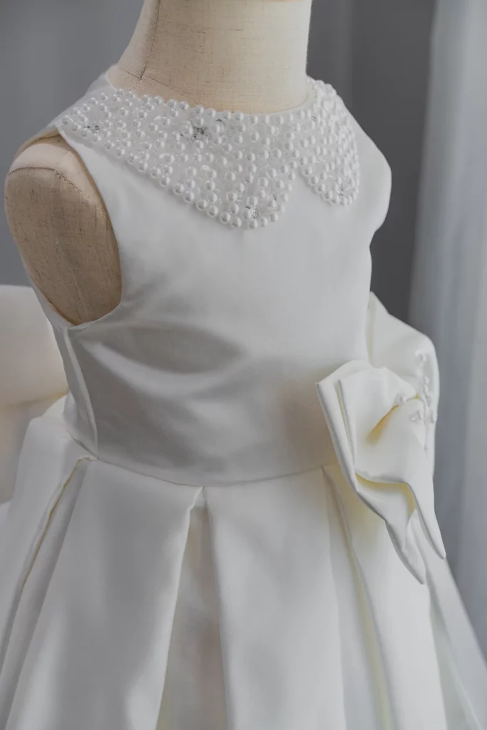 Peter Pan collar dress beaded in pearls with pleating on waist and large bow in ivory color