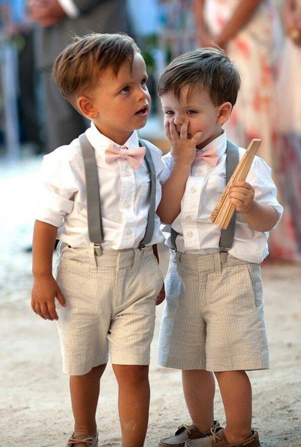 2 little boys in white shirts beige shorts and suspenders with a pink bow tie