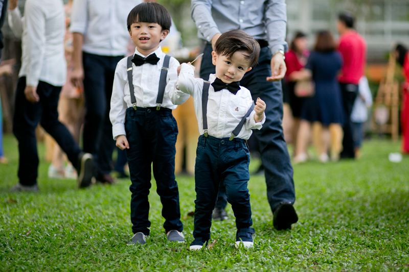 2 little Asian boys in suspenders and bow ties in front of a parent