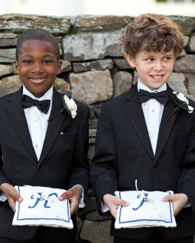 2 older boys in a black tuxedo holding ring cushions